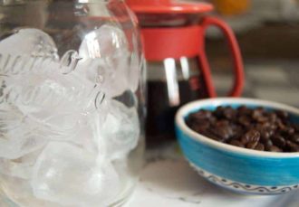 Café recién hecho, vaso con hielo y cuenco con granos de café