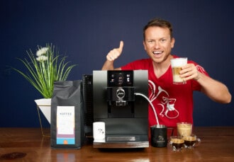 Arne posa sonriente con la cafetera superautomática Jura Z10, un latte macchiato en la mano y un paquete de café de Coffeeness