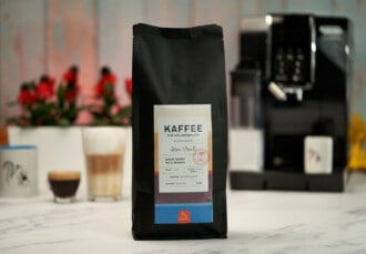Primer plano de un paquete de café de Coffeeness con algunas bebidas preparadas en segundo plano