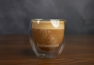 Primer plano de un cortado en vaso de doble pared corporativo de Coffeeness