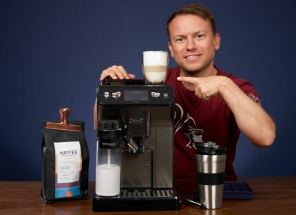 Arne posa con la cafetera superautomática DeLonghi Eletta Explore y un latte macchiato recién hecho